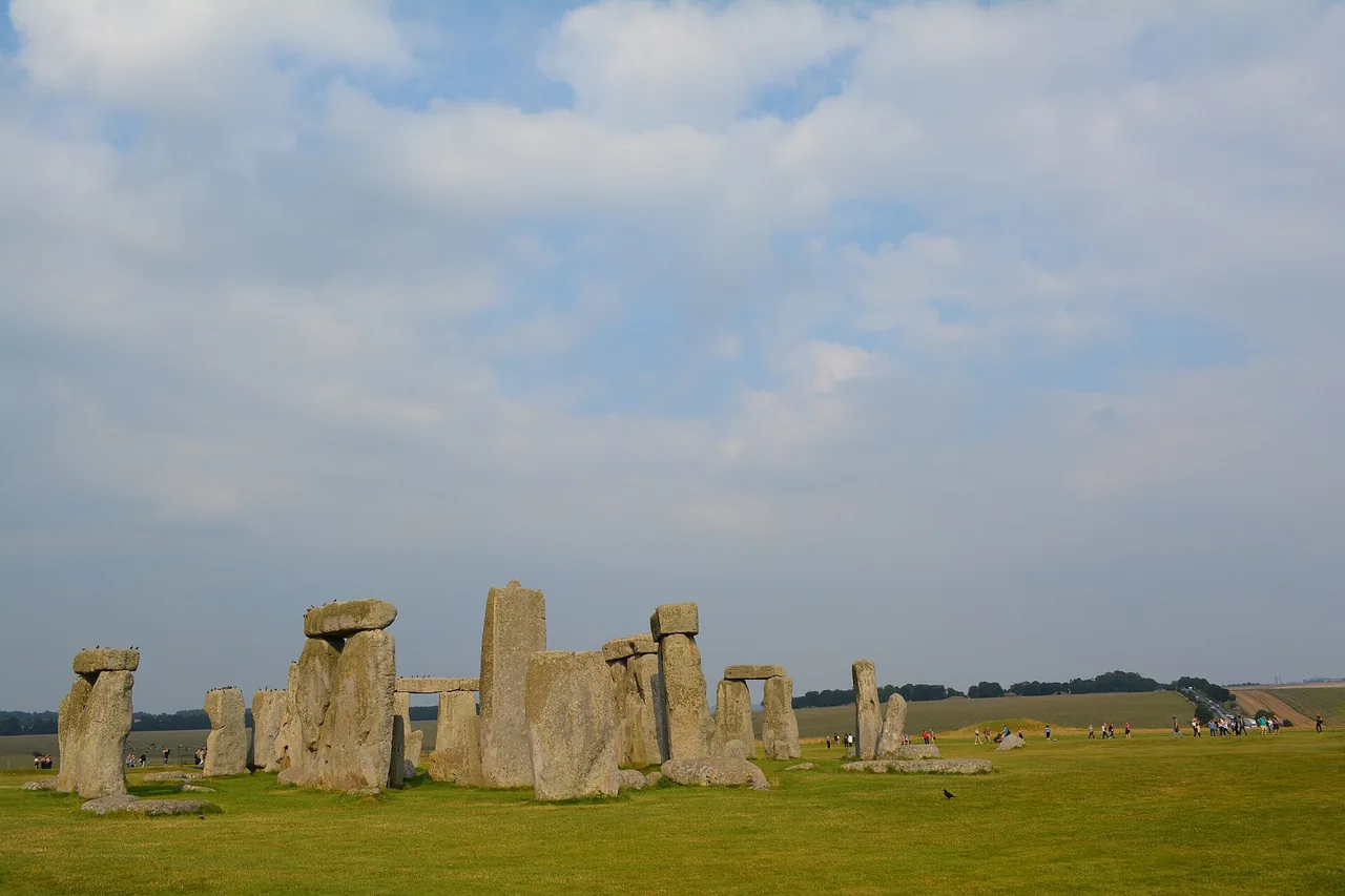 Grey standing stones and lintels of Stonehenge low in the frame on green grass, with a wide sky full of light clouds above.